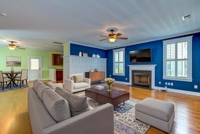 living area with light wood finished floors, a fireplace with flush hearth, visible vents, and ornamental molding