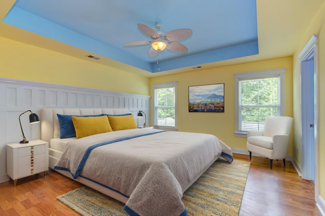 bedroom with multiple windows, light wood-type flooring, and a raised ceiling