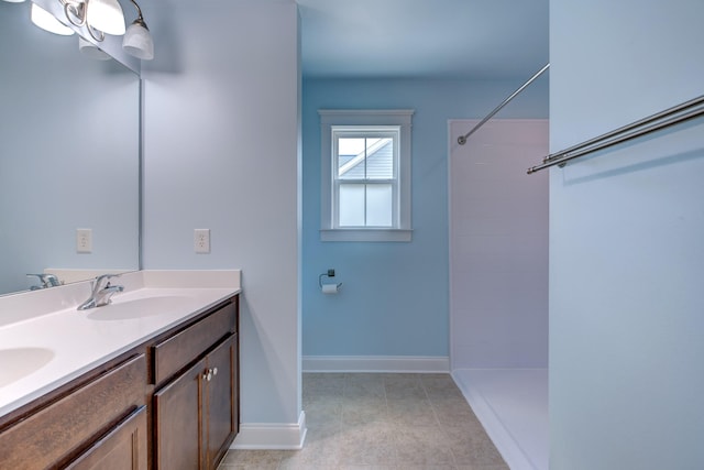 full bathroom with a sink, a tile shower, baseboards, and double vanity