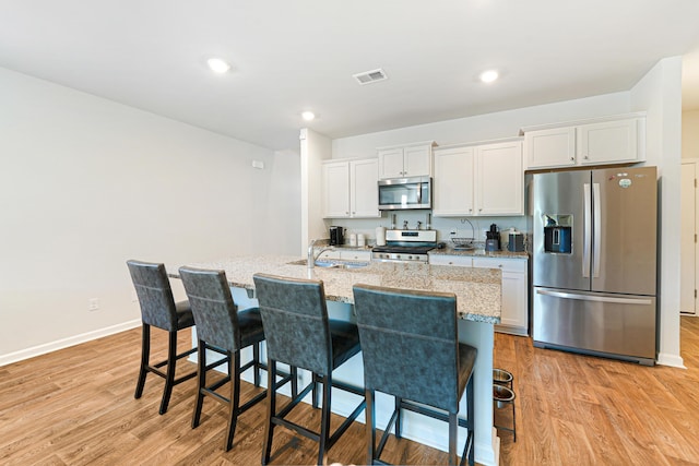 kitchen featuring light hardwood / wood-style floors, white cabinetry, an island with sink, and appliances with stainless steel finishes