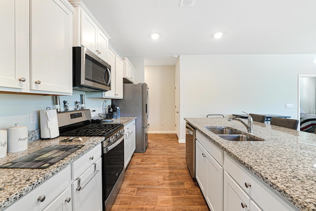 kitchen featuring light stone countertops, appliances with stainless steel finishes, sink, light hardwood / wood-style floors, and white cabinetry