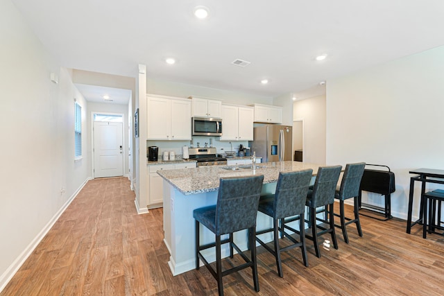 kitchen with a kitchen breakfast bar, appliances with stainless steel finishes, a kitchen island with sink, white cabinets, and light wood-type flooring