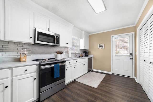 kitchen with appliances with stainless steel finishes, sink, white cabinetry, dark wood-type flooring, and ornamental molding