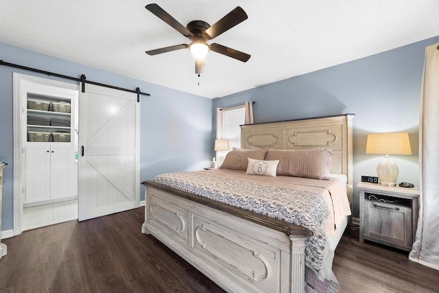 bedroom with ceiling fan, a barn door, and dark hardwood / wood-style floors