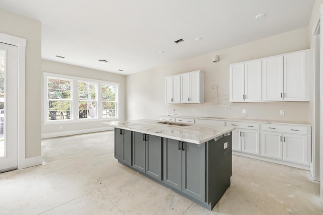 kitchen featuring a center island with sink, gray cabinetry, light stone counters, white cabinetry, and backsplash