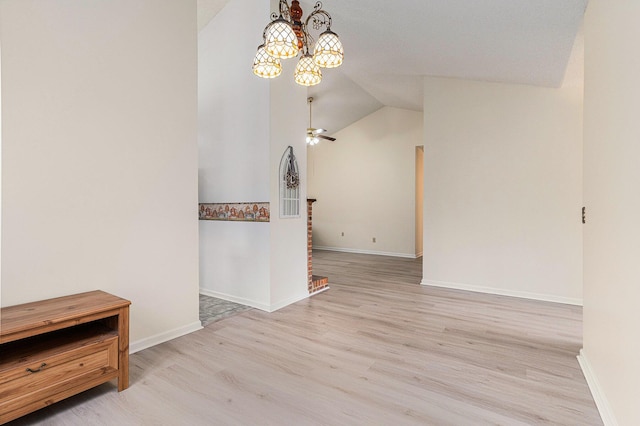 empty room featuring light wood-type flooring, vaulted ceiling, baseboards, and ceiling fan with notable chandelier