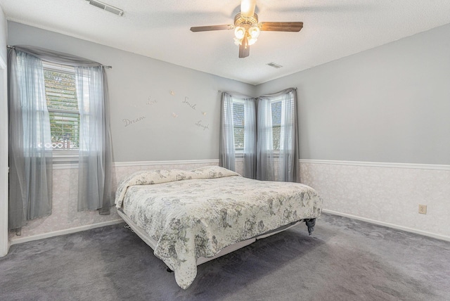 bedroom featuring a textured ceiling, dark colored carpet, wainscoting, and visible vents