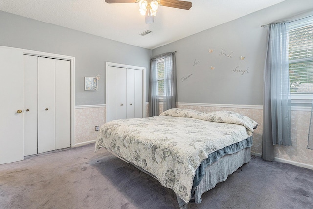 bedroom featuring a wainscoted wall, ceiling fan, two closets, and carpet flooring