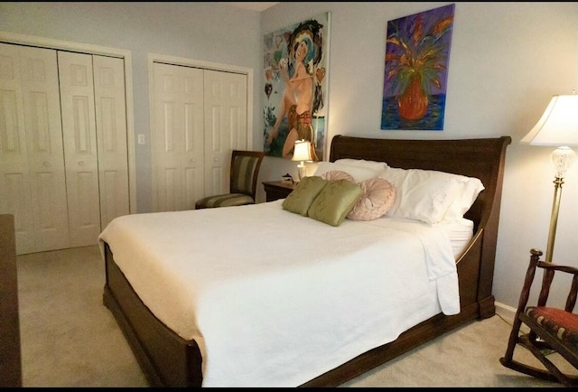 bedroom featuring light colored carpet and multiple closets