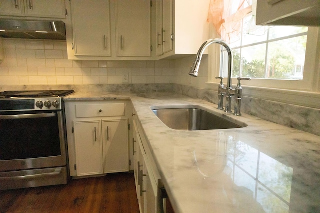 kitchen with stainless steel gas stove, sink, light stone counters, and decorative backsplash