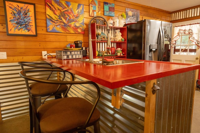 bar with stainless steel refrigerator with ice dispenser, sink, carpet, and wood walls