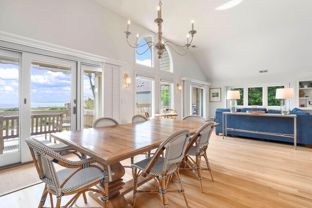 dining space with light wood-type flooring, high vaulted ceiling, a wealth of natural light, and a notable chandelier