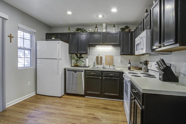 kitchen featuring recessed lighting, white appliances, a sink, light countertops, and light wood finished floors