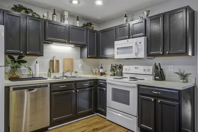 kitchen with recessed lighting, white appliances, a sink, light countertops, and light wood-type flooring