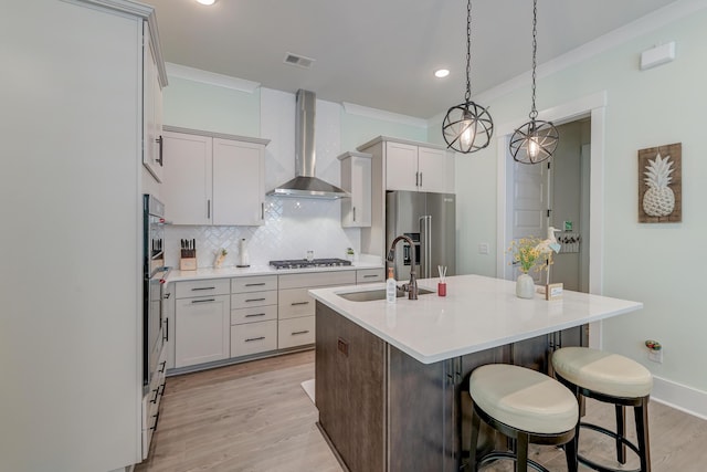 kitchen featuring sink, hanging light fixtures, stainless steel appliances, a center island with sink, and wall chimney exhaust hood