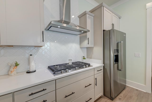 kitchen featuring wall chimney exhaust hood, tasteful backsplash, white cabinetry, stainless steel appliances, and light hardwood / wood-style floors