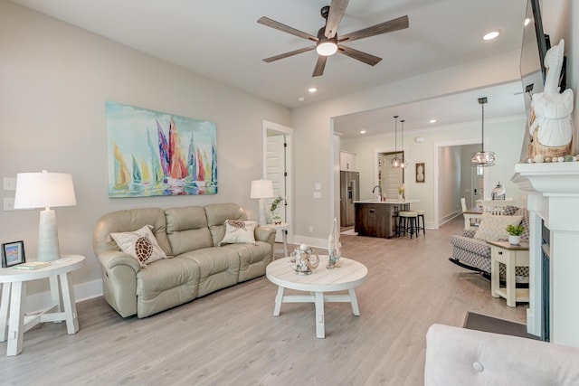 living room with ceiling fan with notable chandelier, a fireplace, and light hardwood / wood-style floors