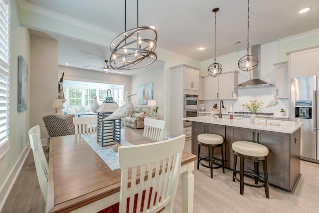 dining room featuring sink, light hardwood / wood-style flooring, ornamental molding, and ceiling fan