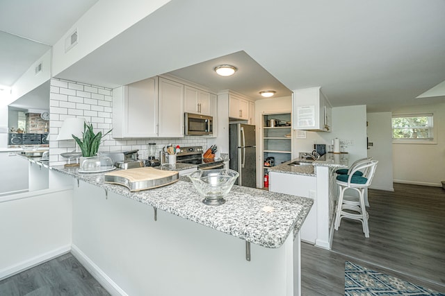 kitchen with a kitchen bar, tasteful backsplash, stainless steel appliances, dark hardwood / wood-style floors, and kitchen peninsula