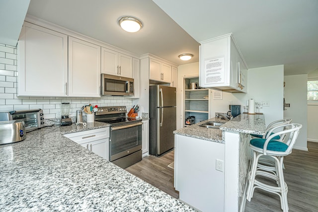 kitchen with light stone counters, light hardwood / wood-style floors, backsplash, white cabinetry, and stainless steel appliances