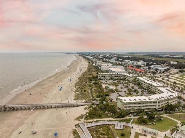 aerial view at dusk featuring a water view and a beach view