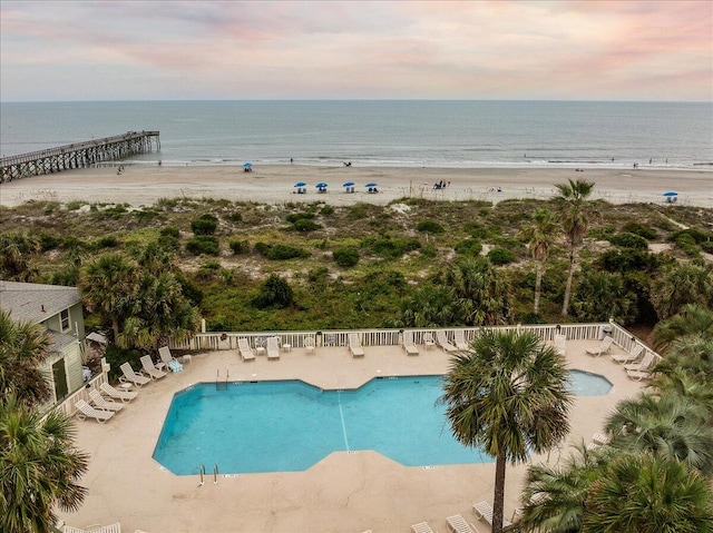 pool at dusk featuring a water view and a beach view