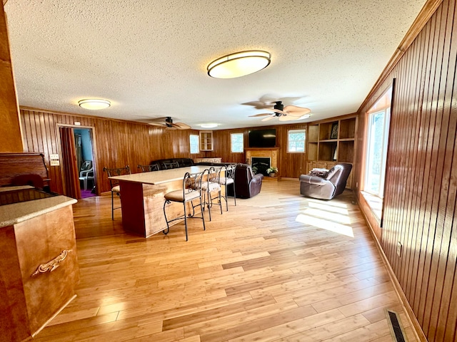 dining area with ceiling fan, a textured ceiling, light wood-type flooring, and wood walls