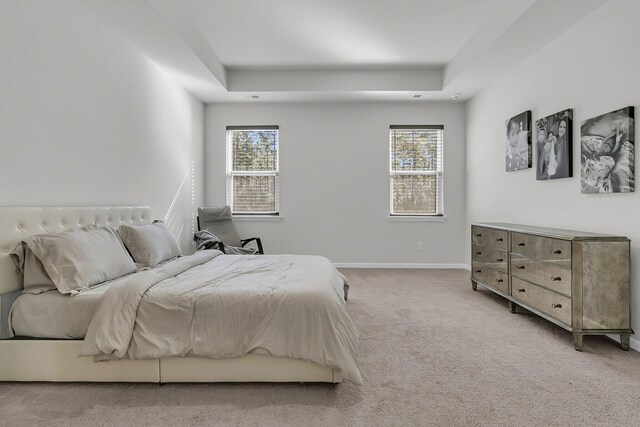 bedroom with light carpet, a tray ceiling, and baseboards