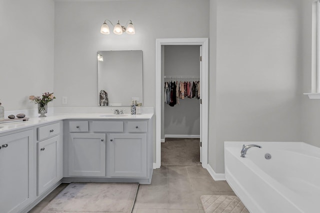 bathroom with vanity, tile patterned floors, a garden tub, a walk in closet, and baseboards
