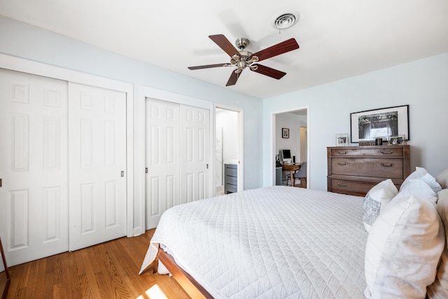 bedroom featuring visible vents, multiple closets, wood finished floors, and a ceiling fan