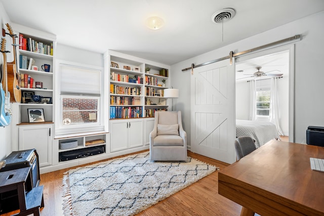 living area with visible vents, a barn door, wood finished floors, and a ceiling fan