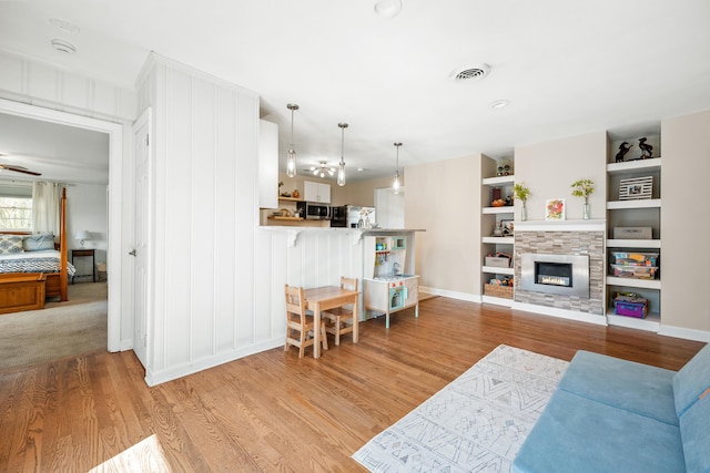 living room featuring light wood finished floors, visible vents, built in shelves, baseboards, and a glass covered fireplace