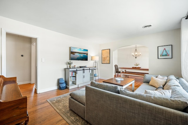 living area featuring light wood-type flooring, visible vents, a notable chandelier, arched walkways, and baseboards