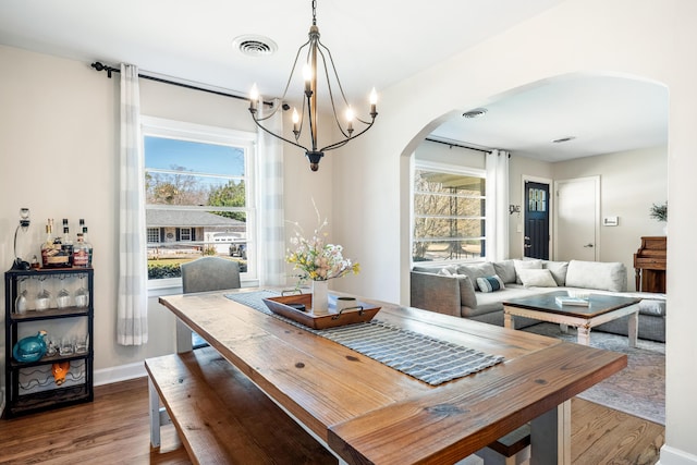 dining room with visible vents, arched walkways, a notable chandelier, and dark wood-style flooring