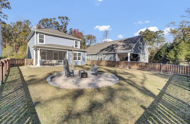 rear view of property featuring a sunroom, a yard, and a fire pit