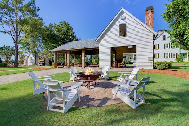 back of property with a lawn, a patio area, and an outdoor fire pit