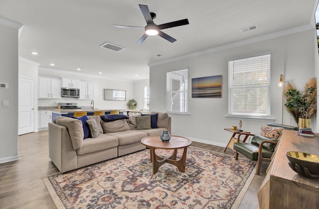 living room with ceiling fan, light wood-type flooring, and crown molding