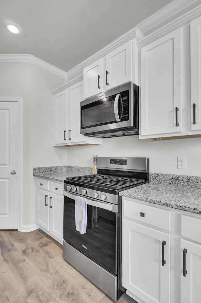 kitchen featuring light stone countertops, white cabinetry, stainless steel appliances, light hardwood / wood-style floors, and ornamental molding