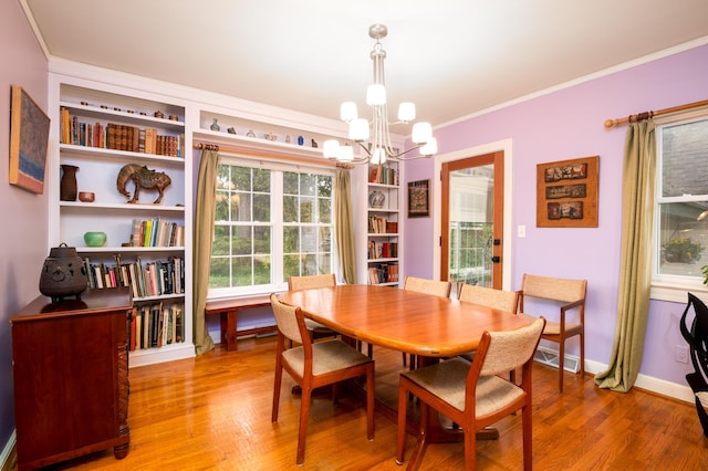 dining room with a chandelier, light wood finished floors, crown molding, built in shelves, and baseboards