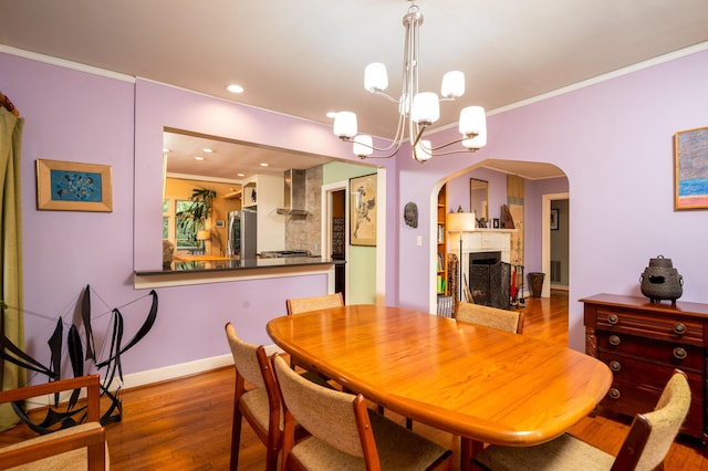 dining room with arched walkways, crown molding, wood finished floors, baseboards, and a chandelier