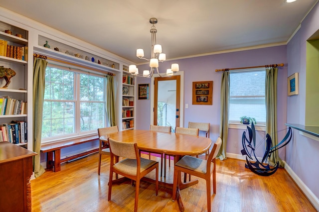 dining room with a chandelier, light wood-type flooring, baseboards, crown molding, and built in features