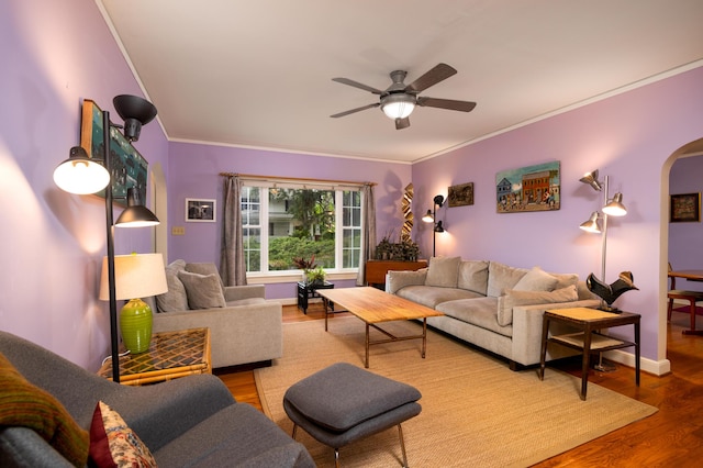 living area with arched walkways, crown molding, wood finished floors, ceiling fan, and baseboards