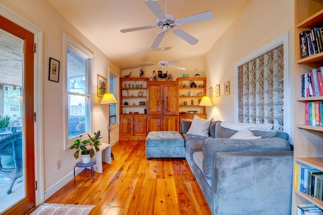 living area with ceiling fan, light wood-style flooring, plenty of natural light, baseboards, and lofted ceiling