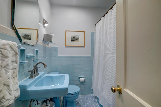 bathroom featuring a sink, toilet, tile walls, tile patterned flooring, and wainscoting