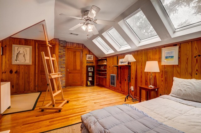 bedroom featuring wooden walls, a skylight, vaulted ceiling, and light wood-style floors