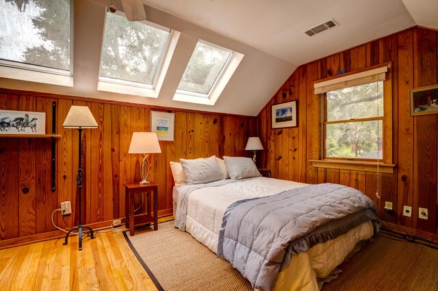 bedroom with vaulted ceiling, wooden walls, wood finished floors, and a skylight