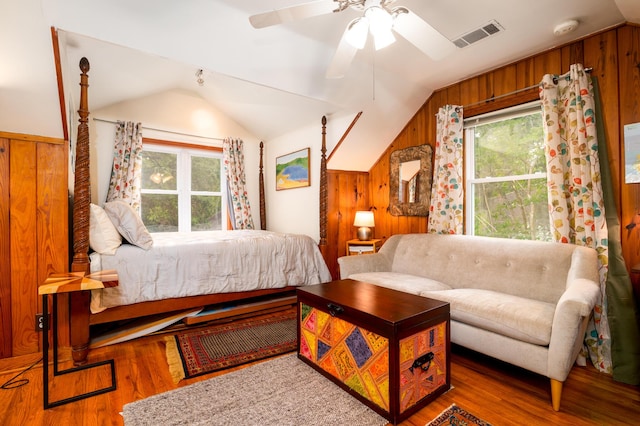bedroom with wood walls, multiple windows, vaulted ceiling, wood finished floors, and ceiling fan