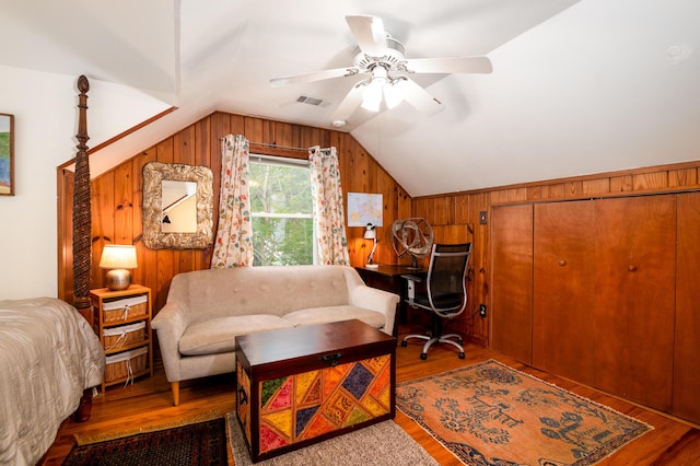 bedroom with vaulted ceiling, wooden walls, wood finished floors, an office area, and ceiling fan