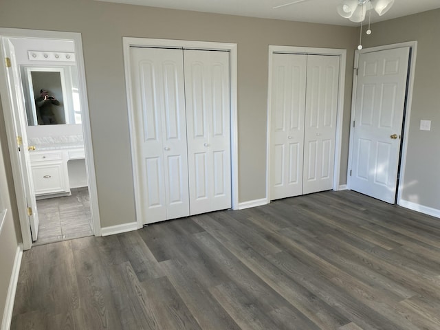 unfurnished bedroom featuring multiple closets, dark wood-type flooring, ensuite bath, and ceiling fan