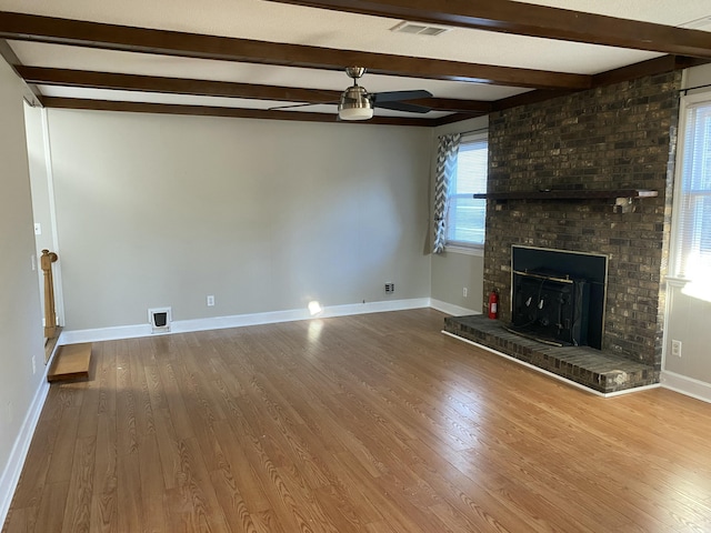 unfurnished living room featuring a brick fireplace, hardwood / wood-style floors, beam ceiling, and ceiling fan